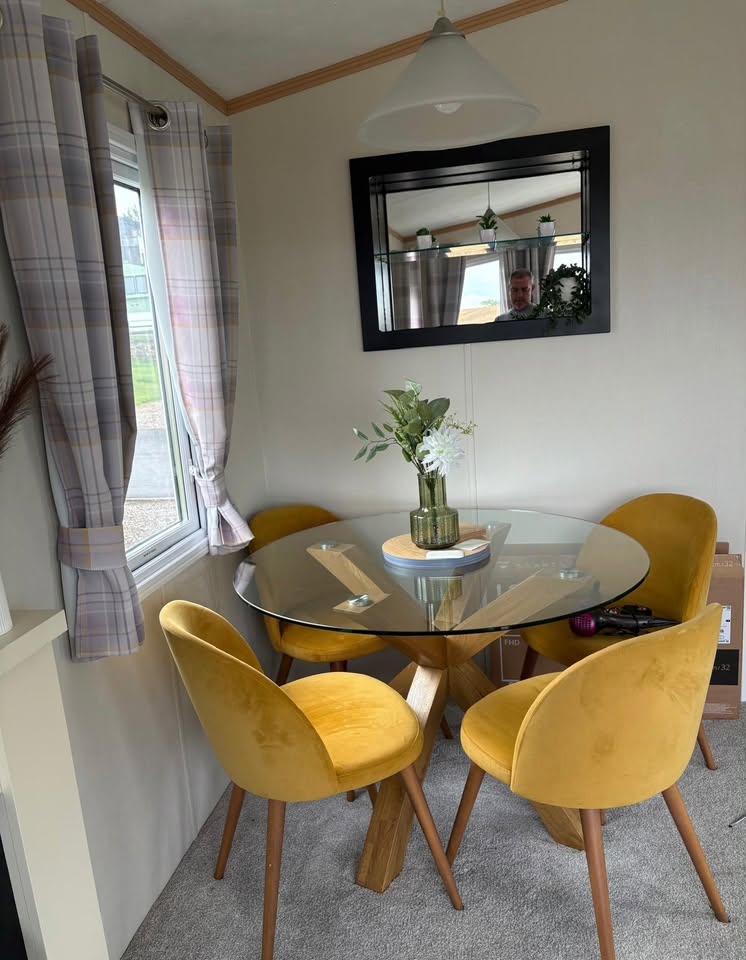 Glass dining table with four mustard velvet chairs beside the window