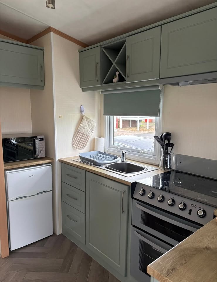 Sage green kitchen with oven, hob, sink and fridge freezer